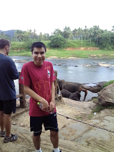 Jorge stands near a river that has elephants near it.