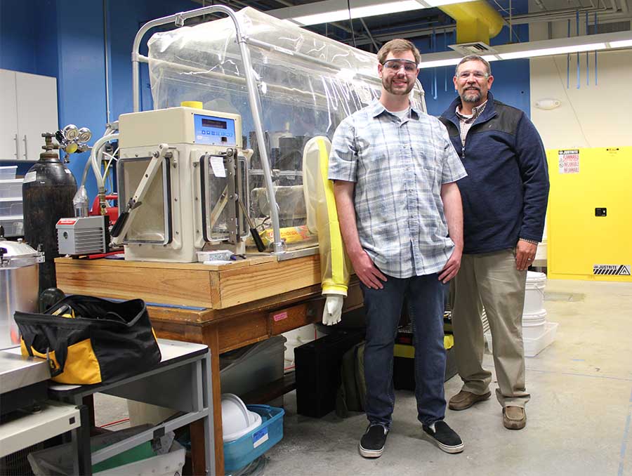 Two men standing in a lab wearing protective glasses.