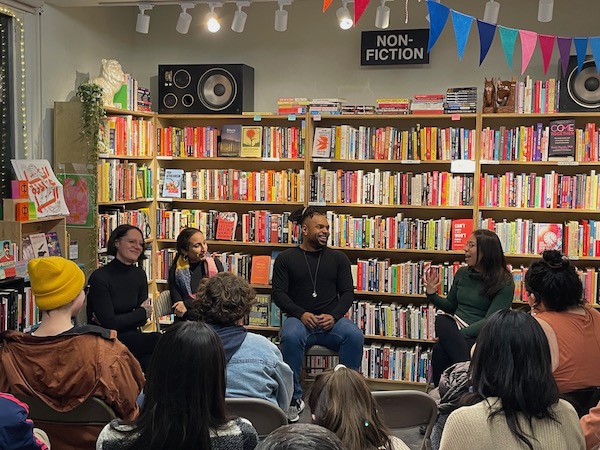 A group of people sit in chairs in a circle in a book store while smiling and talking.