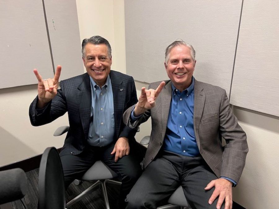 Brian Sandoval sitting next to Gregory Mosier in the podcasting studio holding up wolf pack hand signs.