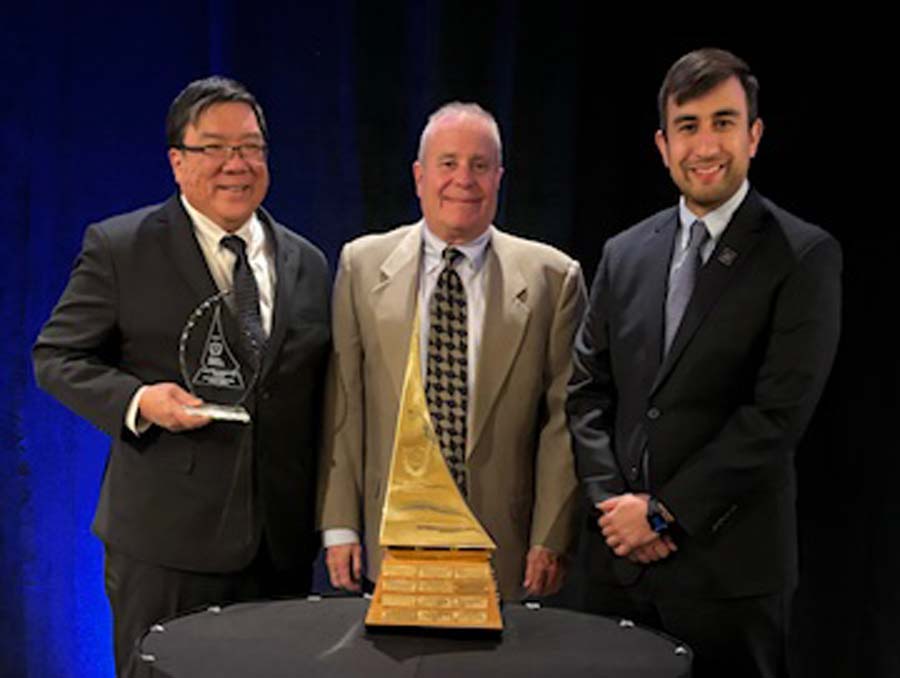 Three people pose for a photo with an award.