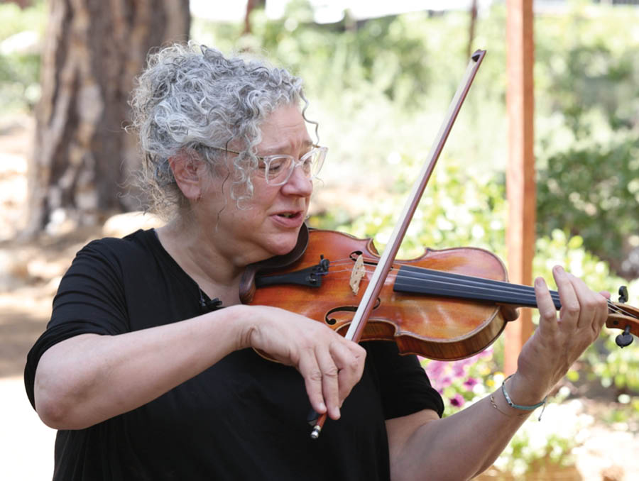 A woman plays the violin on a path in the middle of a forest.