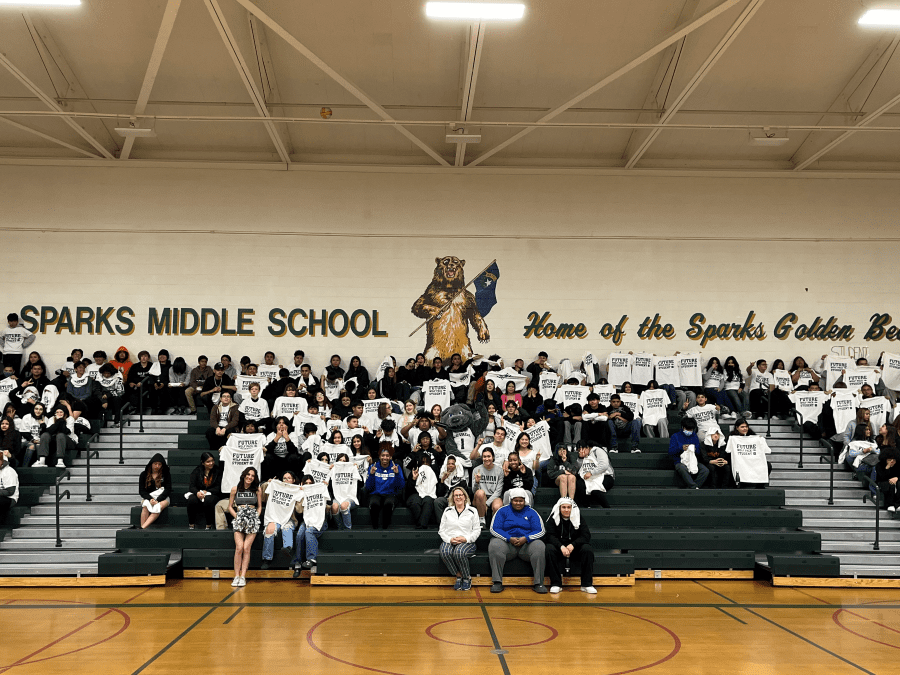 A crowd of students sit on the bleachers in the gym.