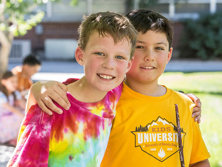 Two boys outside with their arms around eachother smiling.