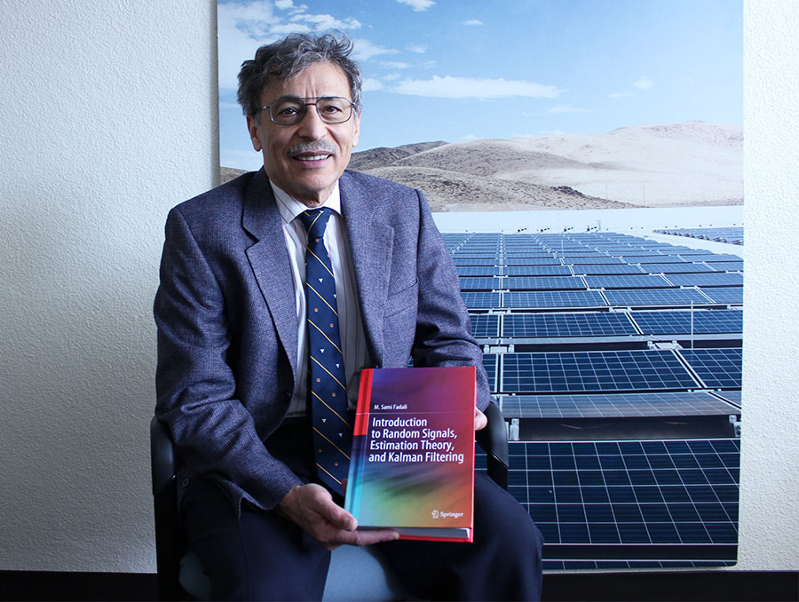 Sami Fadali sitting in a chair holding a textbook.