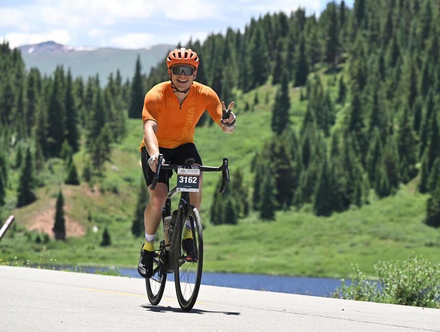 Spencer smiling on a road bike with mountains and pine trees in the background.