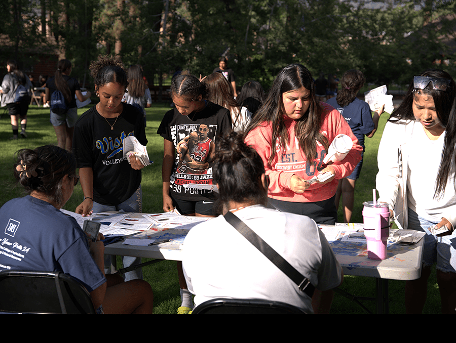 Students grabbing materials at a table.