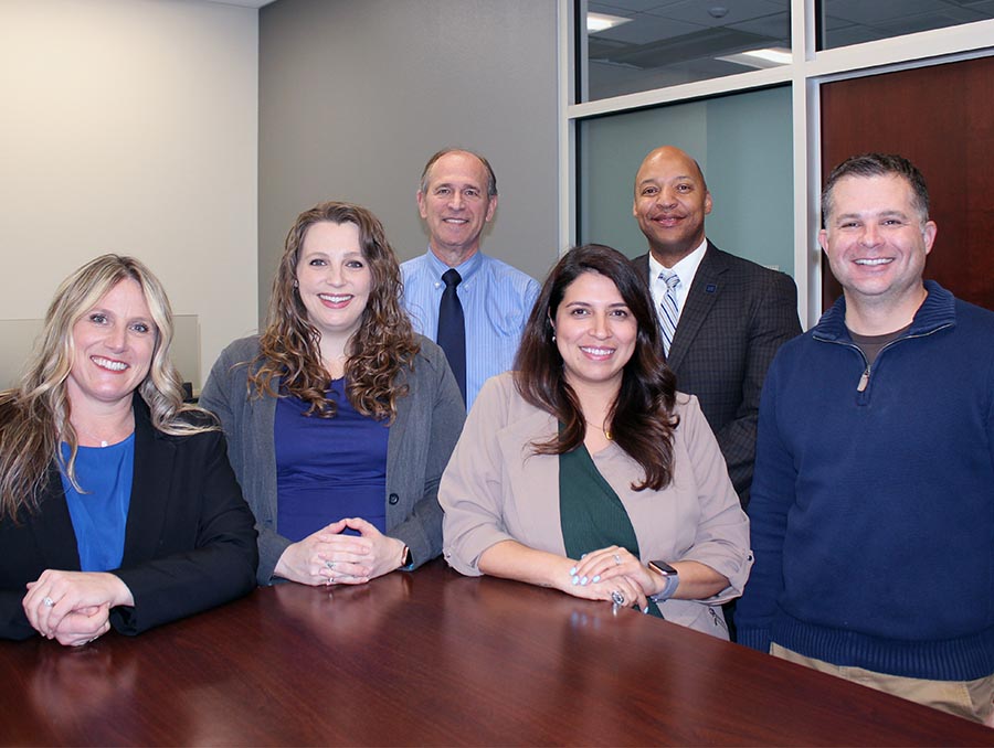 Five current and former Engineering Research Office team members and Dean Erick Jones stand around a table in the Dean's Suite