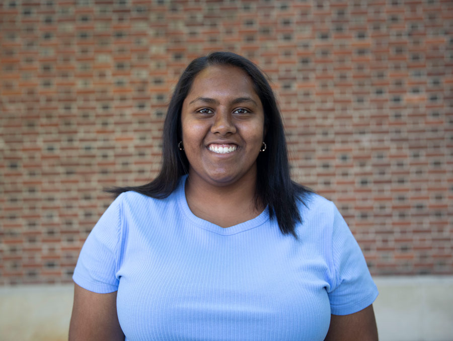 Nandini Naidu smiles in front of a brick wall.