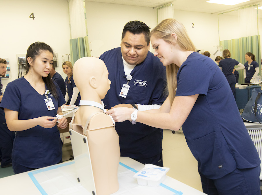 A group of students work on a mock cadaver together and wear Orvis School of Nursing scrubs.