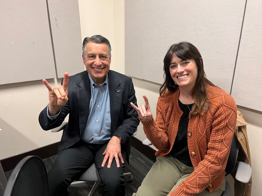 Brian Sandoval sitting next to Phoebe in the podcasting studio holding up wolf pack hand signs.