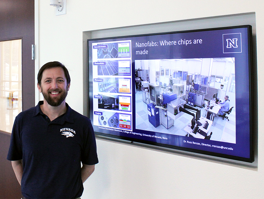 Russell Renzas standing outside the cleanroom next to an electronic screen that reads "Nanofabs: Where chips are made."