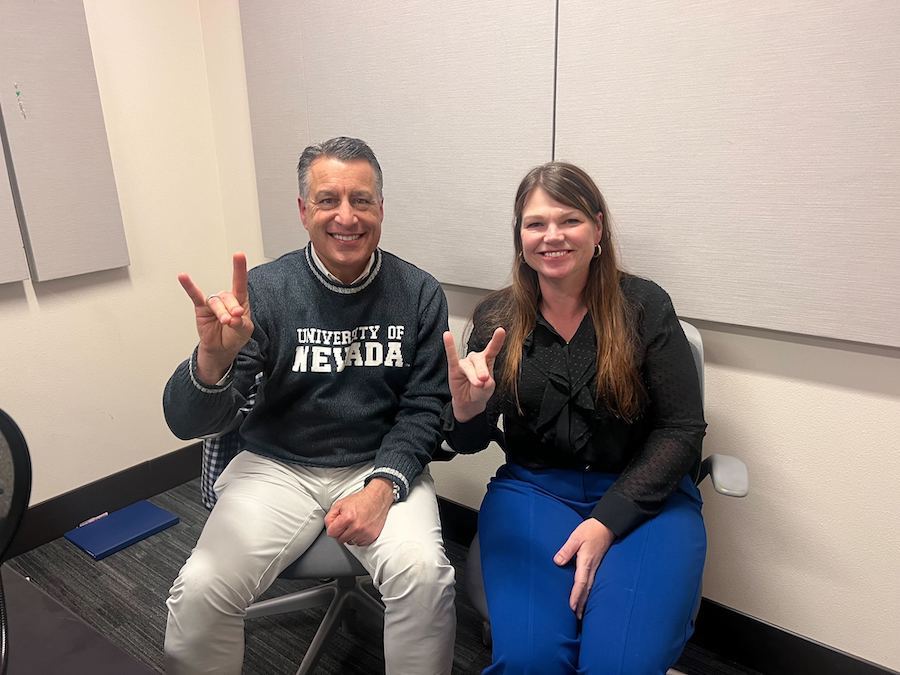 Brian Sandoval sitting next to Louisa Hope-Weeks in the podcasting studio holding up wolf pack hand signs.