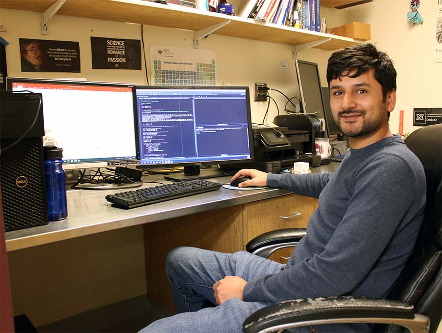 Man sitting in a chair, facing to the left of the frame, in front of a computer desk.