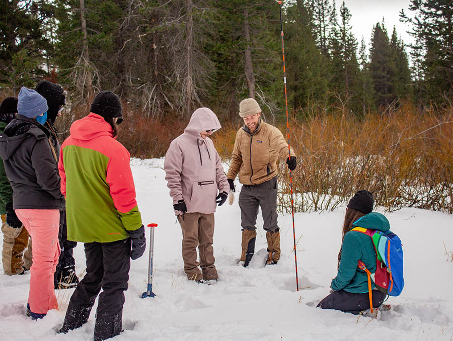 Chris Smith showing students how to take snow pack depth measurements in a meadow