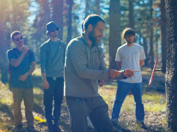 Chris Smith pulls a sample from the core of a tree with students in the background watching.