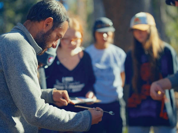 Chris Smith holds a tree sample in front of students in the forest.