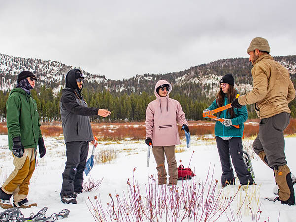Chris Smith standing in a snowy meadow with his students while explaining the lesson.