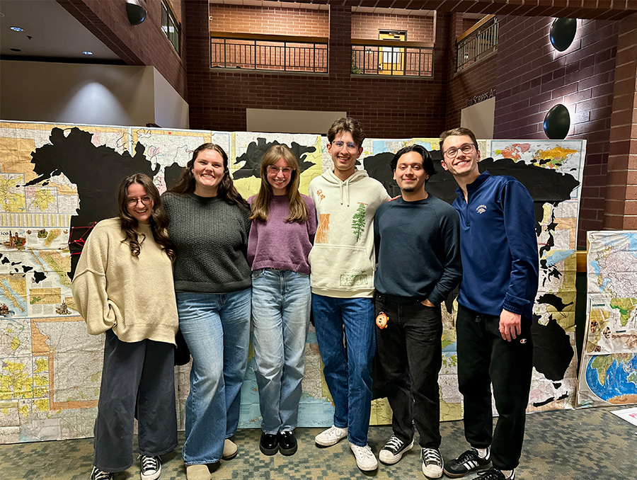 Six students stand in front of their temporary mural depicting a world map.