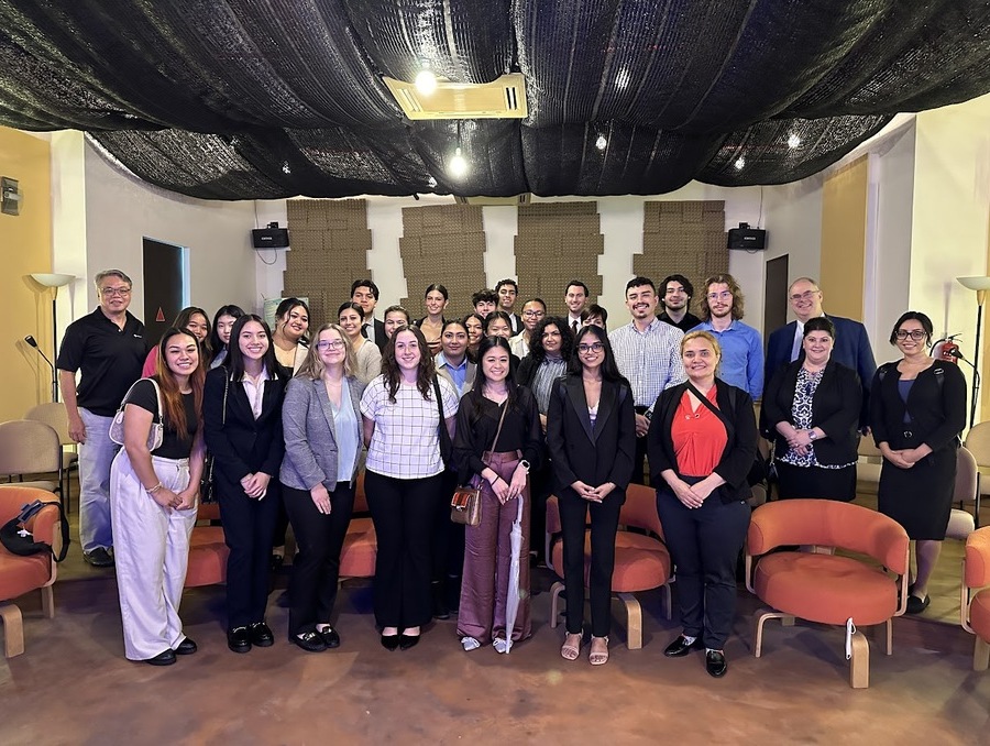 A group of about 30 people in business attire smile for the camera in a meeting or auditorium space.