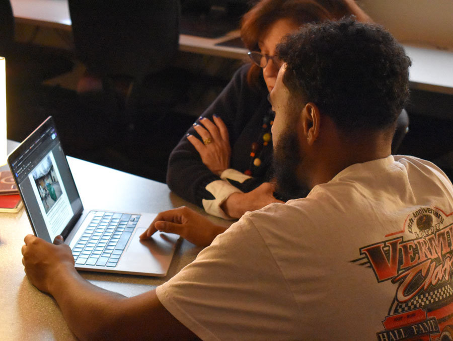 Student and writing coach working together at a desk, reading a writing assignment on the student's laptop. 