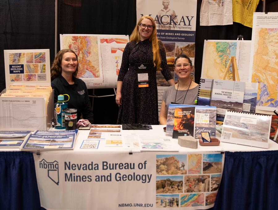 Three women work at a booth surrounded by maps, documents and booklets. They are tabling for the Nevada Bureau of Mines and Geology.