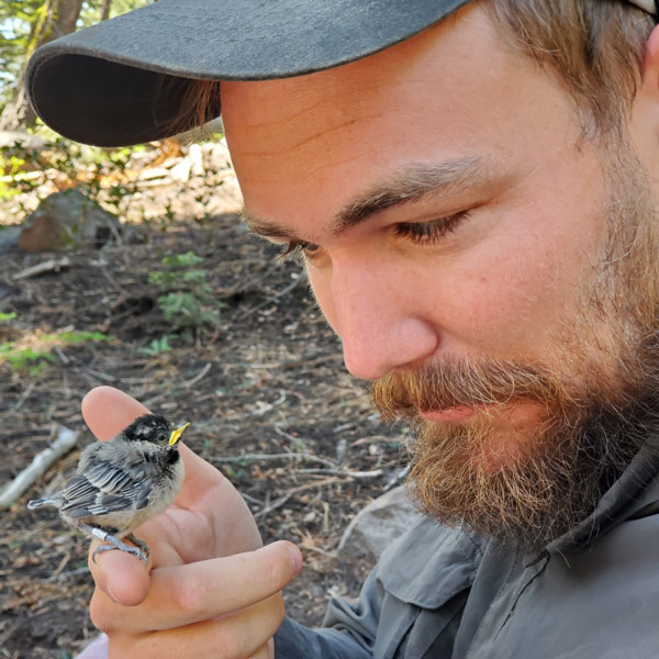 A man wearing a hat holds a baby bird.