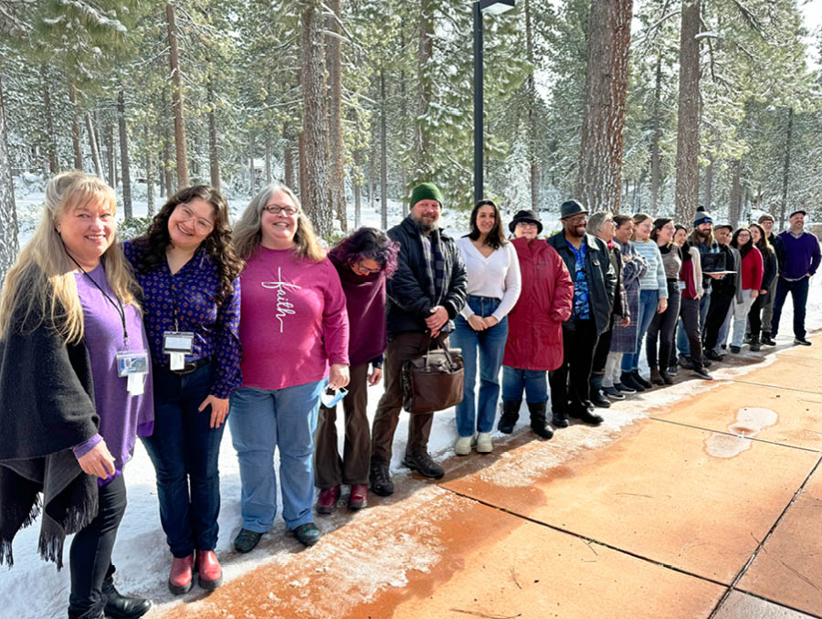 Group of students stand on a sidewalk in front of a winter forest on the University of Nevada, Reno at Lake Tahoe campus.