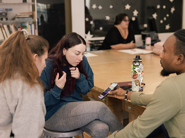 Three Masters in Fine Arts in Interdisciplinary Arts students gather around a phone to discuss how to us ChatGBT in their work.