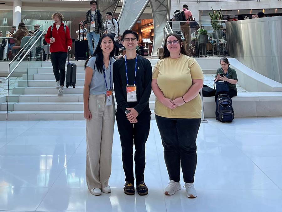 Jennifer Trinh, Antonio Lang and Tara Hartman standing inside a mall or lobby setting with white tiled floors and a set of stairs behind them.