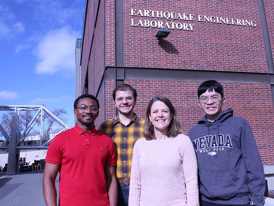 Sir Lathan Wynn, William Roser, Keri Ryan and Yi-En Ji stand in front of the red, brick Earthquake Engineering laboratory