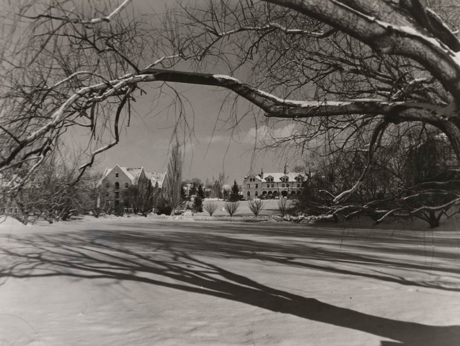A black and white photo of Manzanita Lake covered in snow, with buildings surrounding the Quad in the background.