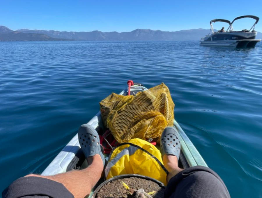 Legs in kayak in Lake Tahoe with snorkeling gear and bags of trash in the front of the kayak.