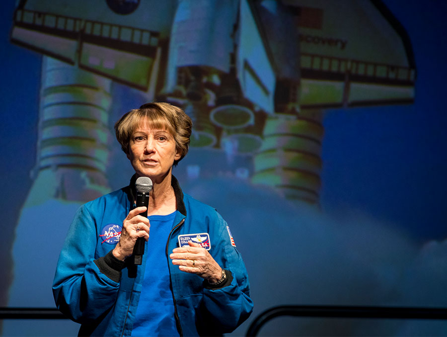 Woman holding a microphone, an image of a rocket in the background.