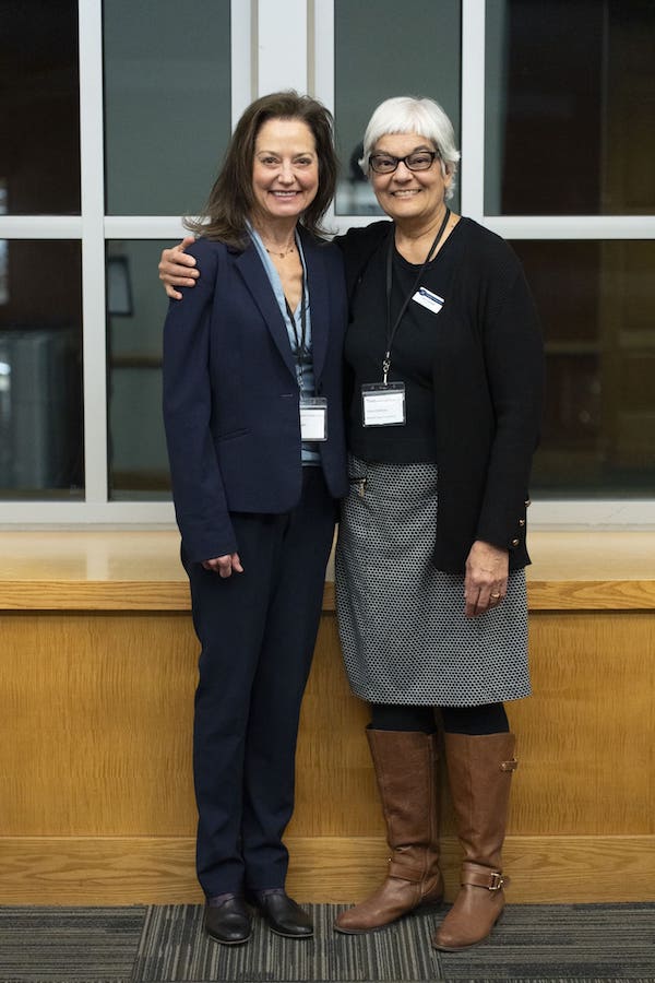 Two women stand and smile at the camera at night inside the Joe Crowley Student Union.