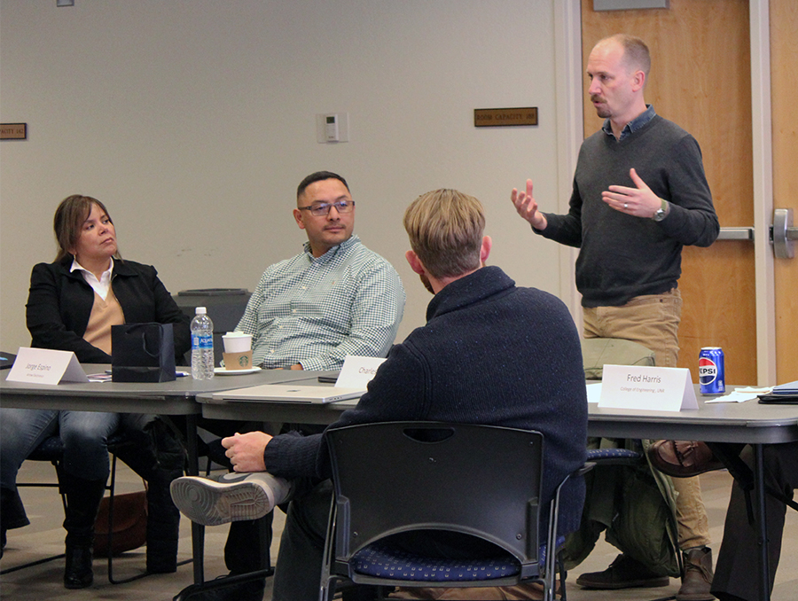 Four people at a table, man on the right standing and gesturing