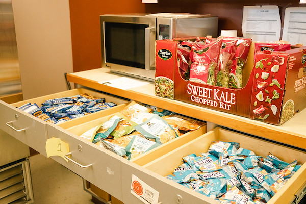 A counter with packaged salads and an open drawer full of healthy pre-packaged snacks.