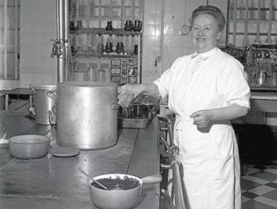 Chef Eugenie Brazier posing for the camera while cooking in a kitchen with large pots