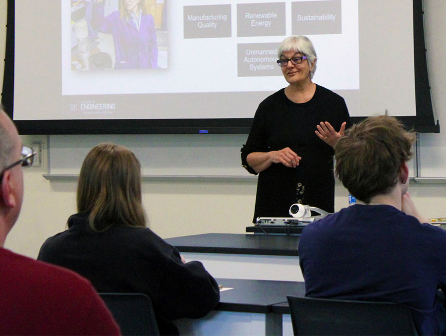 Woman standing in front of project screen speaking to audience.