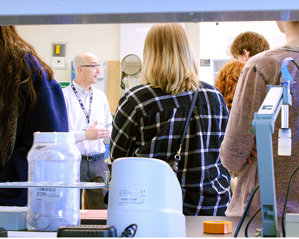 Man standing in a lab talking to a group of people.