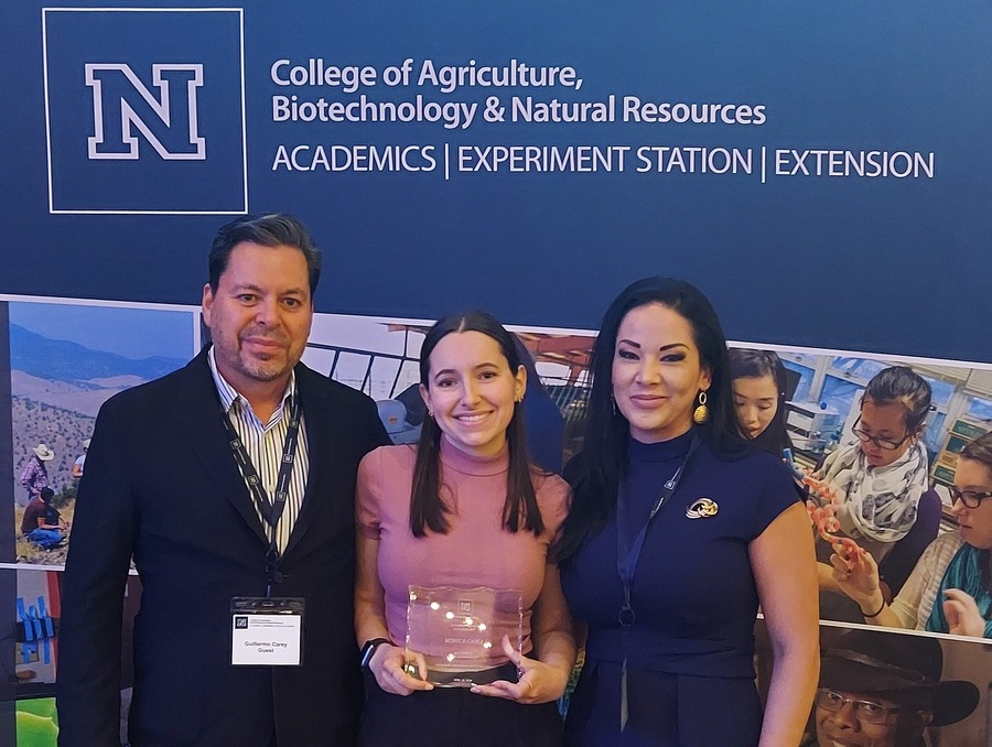 Monica Carey poses with her parents holding an award in front of a sign that says "CABNR Academics. Experiment station. Extension."