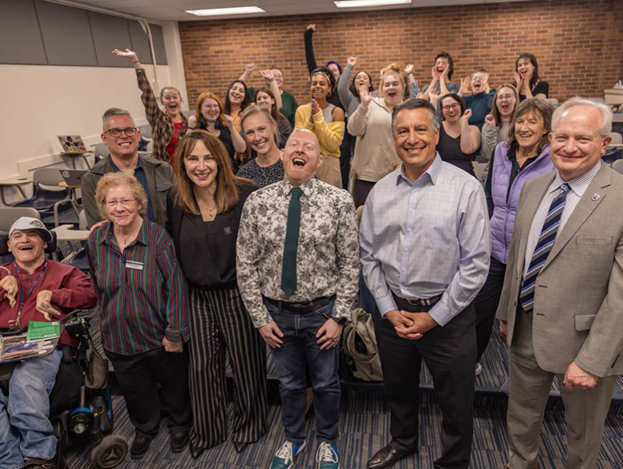 Nate Hodges standing next to President Brian Sandoval, Provost Jeff Thompson, and other faculty, students and colleagues in a classroom.