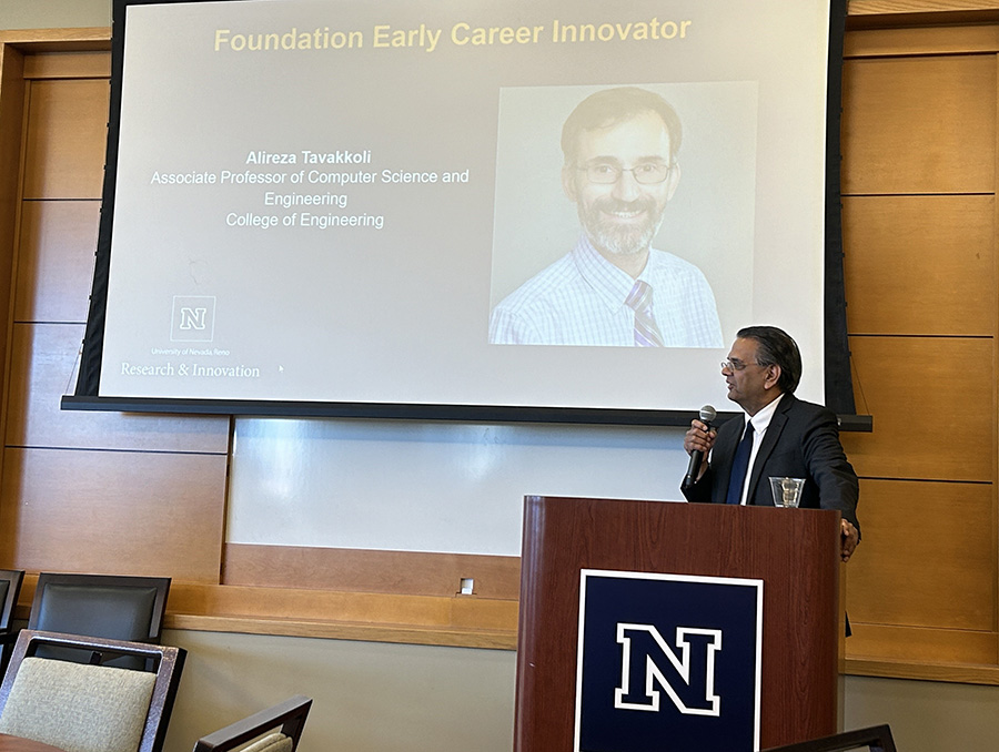 Mridul Gautam speaks at a podium with a power point slide behind him with a photo of Alireza Tavakkoli, Foundation Early Career Innovator