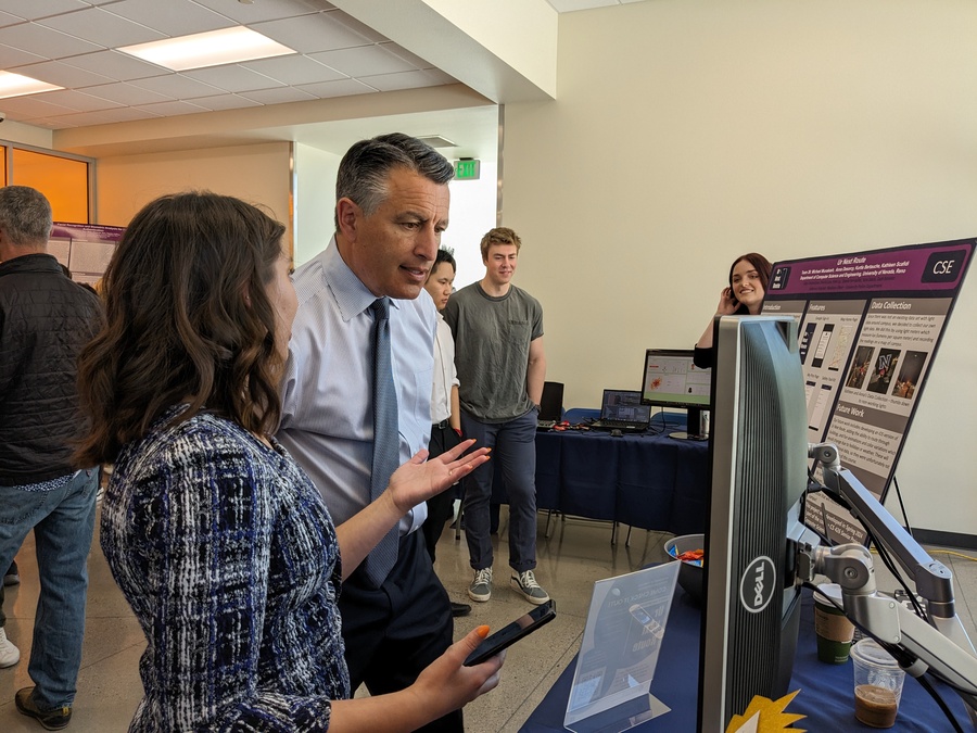 A woman is speaking with President Sandoval as he looks at a poster explaining the safety app.