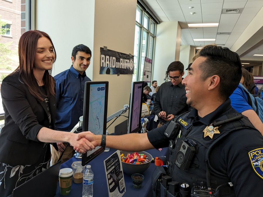 A student shakes hands with a University police officer across a table during a tabling event where the app is on display.