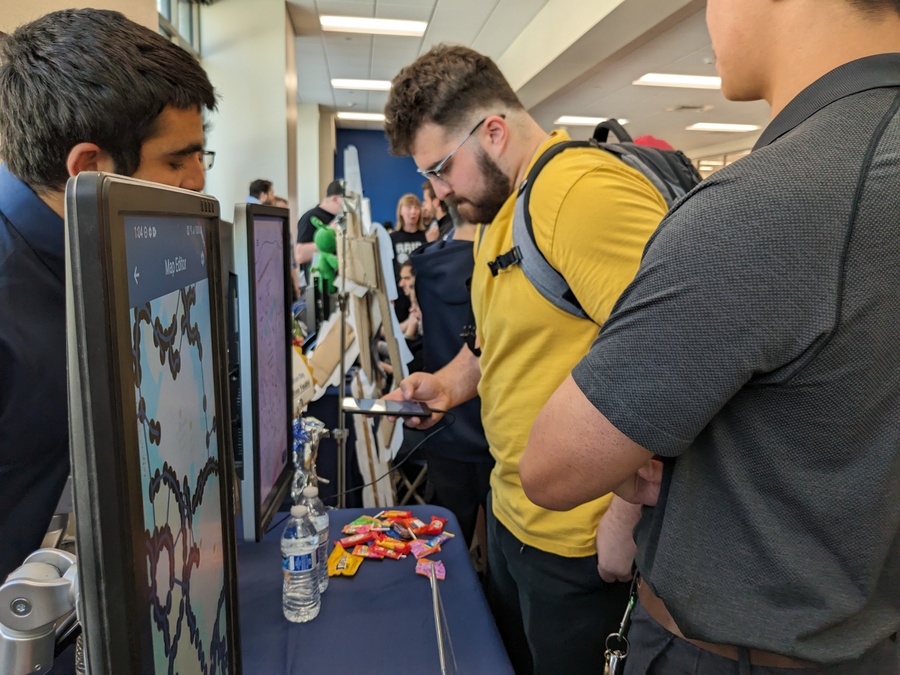 Students looking at the app on a phone at the booth during Innovation Day.
