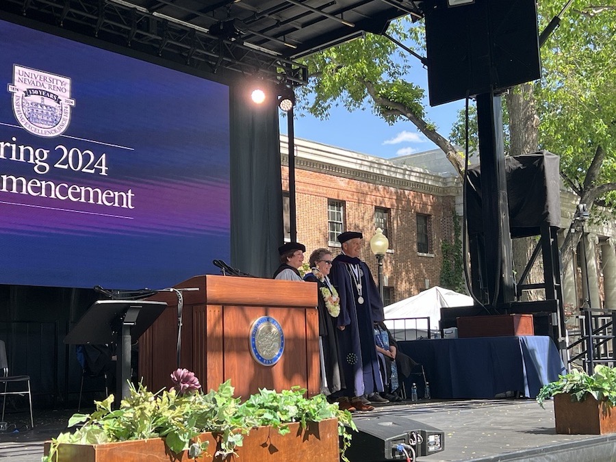 Margaret Cavin stands on the spring commencement stage alongside Brian Sandoval and Regent Del Carlo.