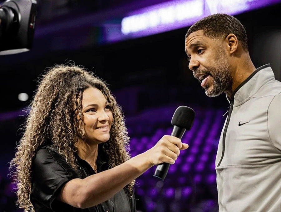 Gianna Hearn holding a microphone up during an interview with a basketball coach.