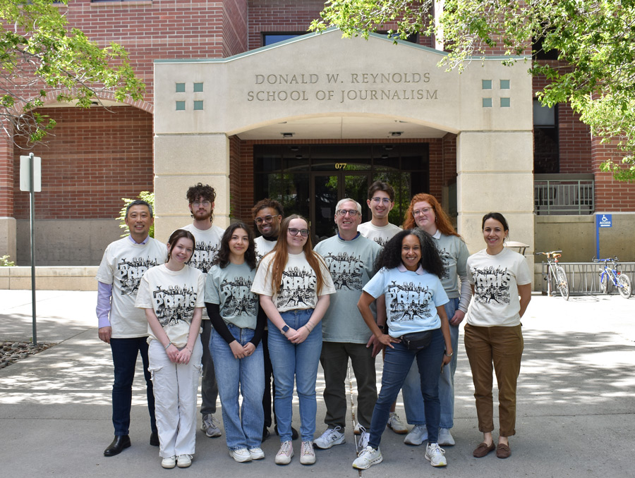 A group of students and faculty standing out in front of the Reynolds School building wearing matching Paris t-shirts.