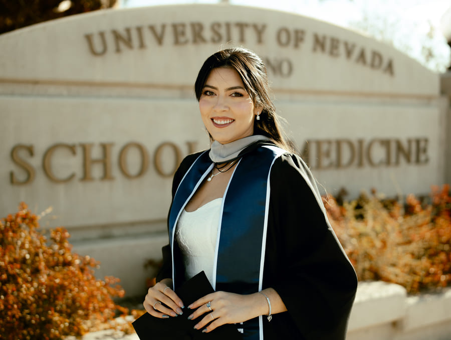 Valeria Savage in her graduation gown standing in front of the School of Medicine sign.
